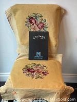 Two vintage hand embroidered floral textile pieces displayed draped over a chair showing front side embroidered floral designs.