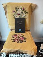 Two embroidered floral textile pieces displayed draped over chair, showing front and back sides