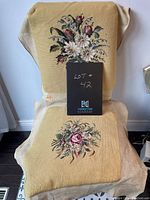 Full view of two embroidered floral pieces displayed on chair and draped over surface, showing colors and design.
