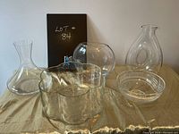 Full lot of glassware displayed together showing two decanters, two vases, and two bowls on a gold-colored satin cloth.