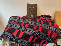 One textile spread out showing plaid pattern in black, red, purple and blue colors.