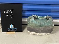 Full view of the Japanese ceramic box showing its curved shape, patina finish, and bamboo-style lid handle.