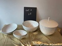 Lot of white serving dishes including bowls and plates with subtle grey line pattern, displayed on gold cloth
