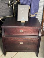 Night table with two drawers, dark brown wood, square metal handles, visible surface wear.