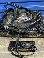 Black leather Danier handbag with shoulder strap and matching wallet on a beige cloth against a blue background. The bag features a snake skin texture and metal feet at the bottom.