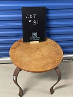 Front view of round side table showing wood veneer top and curved iron legs, with a sign in the background