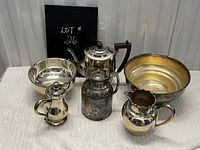 Wide shot showing all five silverplate items including bowls, teapot, creamer, and pitchers on a white cloth