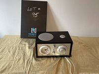 Front perspective view of the Tivoli Audio Model Three radio with wooden casing, top speaker, and control panel with knobs and dials visible.