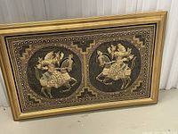 Frontal view of the framed vintage Thai tapestry showing two embroidered figures on horseback in circular frames, set in a gold-tone frame.