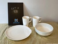 Front view of white bowl, white plate, and two textured white coffee mugs against a neutral background.