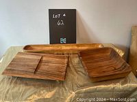 Photo showing three wooden serving dishes on a table: a long bread server, a rectangular divided cheese plate, and a square salad plate.