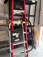 Full view of the red ladder leaning against shelving with the black and silver step stool attached or in front