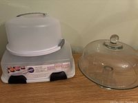 Wilton 3-in-1 Cake Caddy carrier with plastic dome lid and gray locking side clasps alongside a glass cake dome with knob handle.