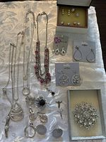 Photo showing assortment of necklaces, earrings, rings, and a brooch spread on fabric background