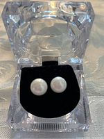 Pair of white cultured pearl stud earrings set in sterling silver displayed in a clear acrylic box with black velvet interior holding them upright