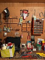 Wide view of pegboard wall with hand tools hanging, box of tapes, containers, and other hardware visible on work surface below.