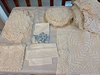 Wide view of assorted handstitched crochet doilies, table runner, and embroidered linens laid out on a flat surface
