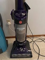 Front view of upright Hoover WindTunnel vacuum showing full body, canister, and power cord on floor.