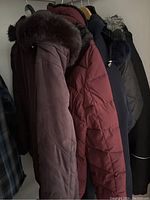 Photo of multiple ladies' jackets hanging on a rack showing fur-trimmed hoods and quilted outerwear.