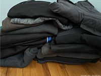 Stack of men's activewear clothing mostly in dark colors, folded, showing a variety of fabric textures and styles.