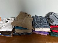 Image showing four vertical stacks of folded men's long sleeve button-up shirts in various colors including white, beige, blue, purple, plaid, and other shades.