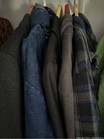 View of five men's jackets hanging on wooden hangers showing fabric and color variety