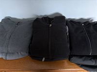 Three folded men's hoodies side by side - gray, black, and darker gray
