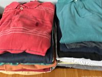 Two stacks of folded men's short-sleeve shirts showing variety of colors including coral pink with stripes, teal, orange, black, white.