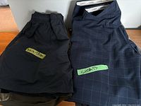 Top view of folded black swim trunks and navy blue shorts with grid pattern, labeled respectively with tape.