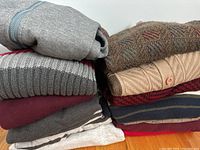 Stack of folded men's sweaters and a hoodie in various colors and patterns, sizes Large/XL.