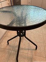 Full view of round bistro table showing textured tempered glass top and tripodal aluminum base