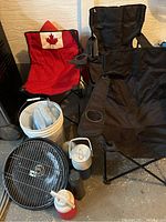 Three collapsible chairs (one red with Canadian flag, two black), charcoal grill components, white pail with blue ice packs, and thermoses.