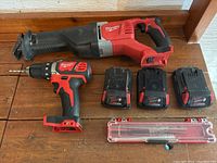 Overview showing reciprocating saw, drill/driver, three batteries and blade case on wooden surface