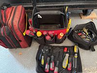 Shows the Husky toolbag filled with screwdrivers, additional red bag, and extra worn black bag on garage floor.
