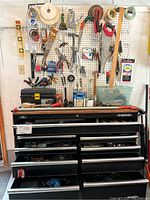 Wide view of a Husky tool chest with multiple drawers and a white pegboard above it holding various hand tools including hammers, pliers, saws, tape measures, and brushes.