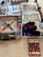 Vintage toys and puzzles laid out on carpet including board games, puzzles, slippers, small toy car, and Chess book.