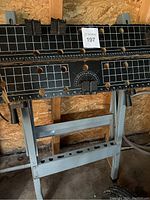 Full view of metal work bench with black clamping surface marked with white grid and measurements, supported by metal frame.