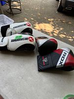 Two pairs of boxing gloves on a table, with one pair of white and black Kimurawear gloves and one pair of black, red, and white RDX gloves.
