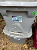 Photo showing two gray Sterilite storage totes stacked outdoors on ground, with visible label and normal wear including dents and surface marks.