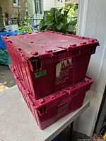 Two stacked red plastic totes with lids. One lid repaired and shows edge wear.