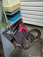 Bike trailer folded and leaning against wall with visible two wheels, metal frame, and fabric storage area.