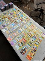 Wide view of Pokémon cards laid on a table, showing many character cards with yellow borders and visible normal wear.