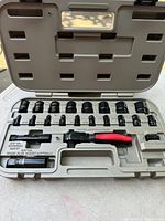 Opened case showing ratchet wrench with red and black handle and various sockets and adapters arranged in molded slots.