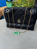 Front exterior view of black quilted Kate Spade purse with gold chain shoulder strap and turn-lock clasp.