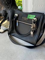 Exterior front view of the black Guess purse with attached metal charms and shiny hardware.