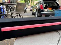 Close-up photo of the Monster sound bar with the LED strip glowing red, placed on a table outdoors with cars and chairs in the background.
