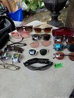 Lot of several pairs of sunglasses and eyeglasses on a table outdoors, various styles and lens colors.