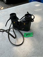 Full view of black Nikon binoculars with attached neck strap placed on a flat surface.