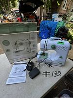 White Singer QuikFix sewing machine with green controls, power adapter, foot pedal, instruction manual, and original box on a table.