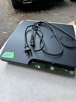 Sony PS3 console with power cable on top, shown from an angle highlighting front power button and console surface.